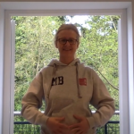 woman standing before open door with hands over stomach preparing for a breathing exercise