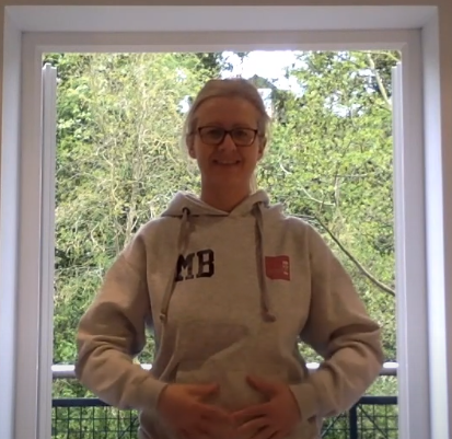 woman standing before open door with hands over stomach preparing for a breathing exercise
