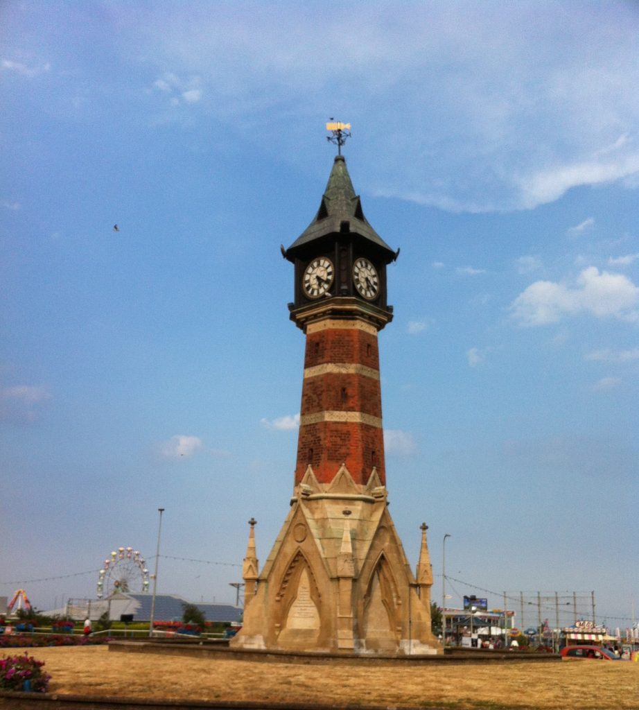 clock tower at Skegness, grey pointed top above hte clock, orange brick tower, whit stone decorated base