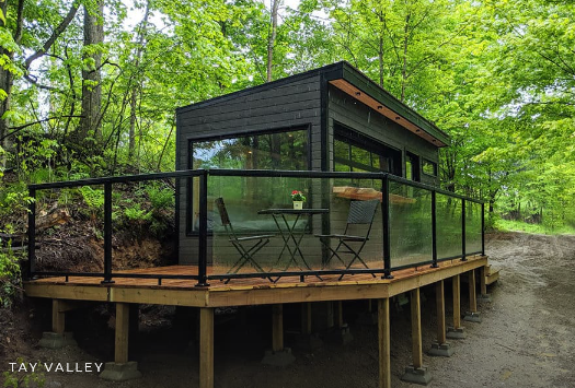 A wooden hut with lots of glass on a wooden platform in the middle of a forest