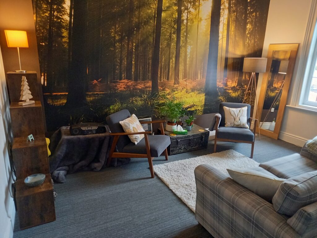 Therapy Room with sofa, 2 chairs, forest wallpaper and a lamp. This is the office of Counselling West Bridgford