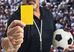 Football referee holding up yellow card and football under arm