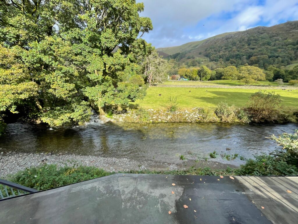 River in the foreground with tree field and hill in the distance with blue sky