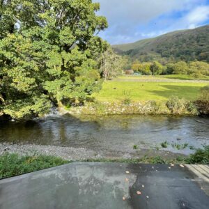 River in the foreground with tree field and hill in the distance with blue sky