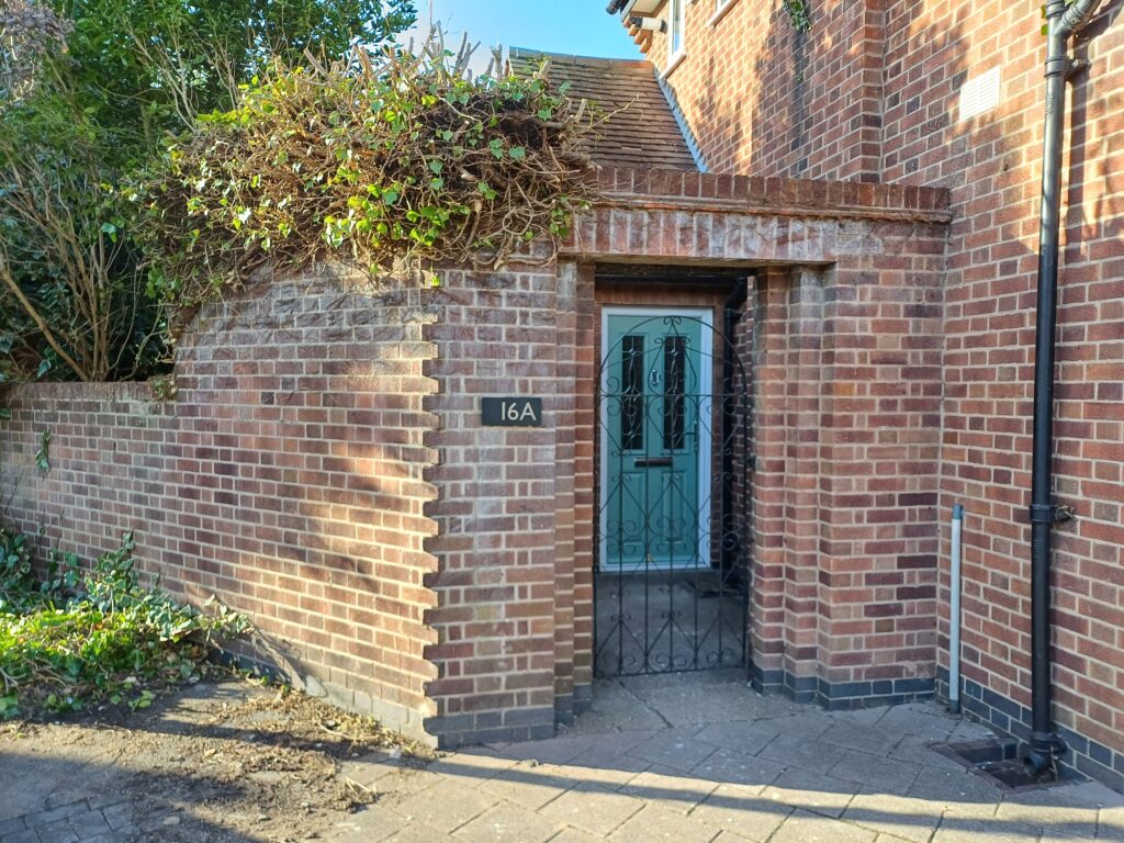 photograph of green front door showing through high wall with 16A sign on the wall