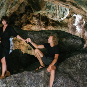 couple in a cave man reaching out to woman to help climb over rocks