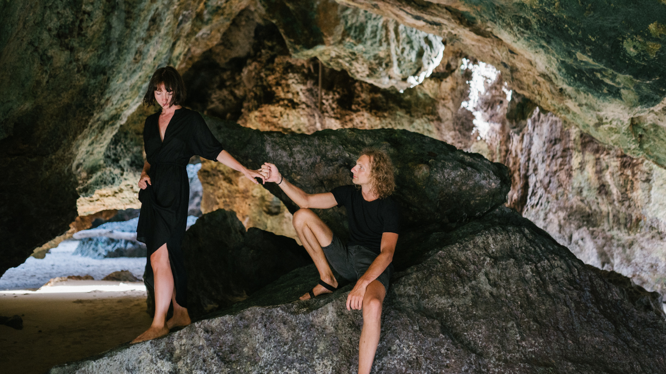 couple in a cave man reaching out to woman to help climb over rocks