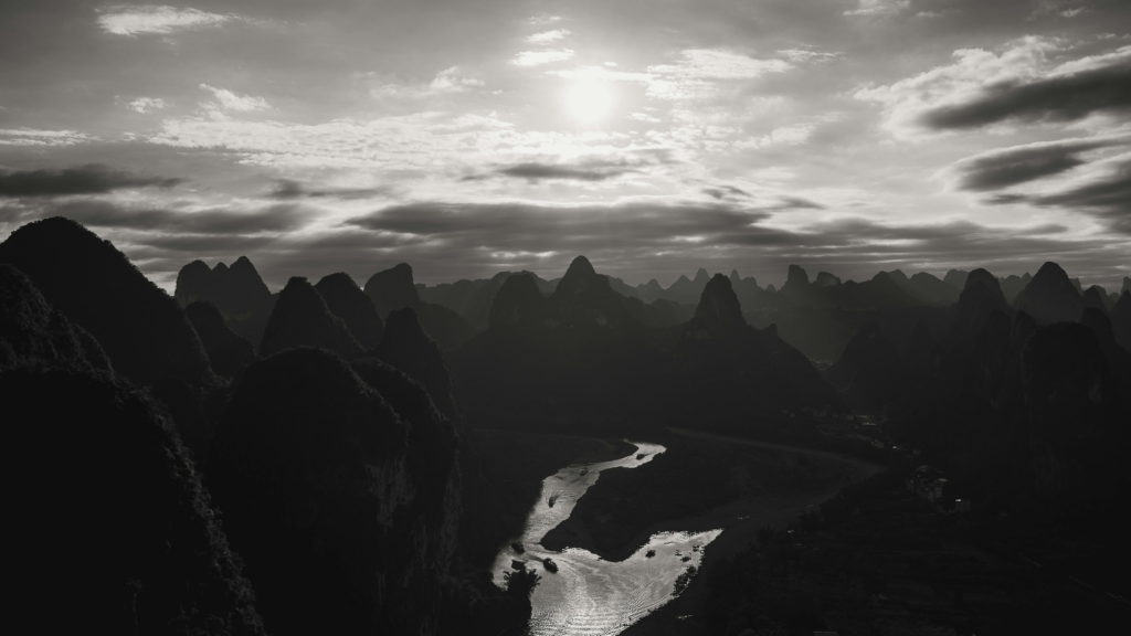 Why we lie. Black and white photograph of valley, sky light clouds and sun glimmering through
