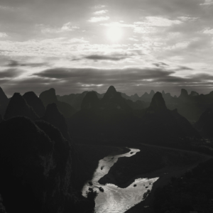 Why we lie. Black and white photograph of valley, sky light clouds and sun glimmering through