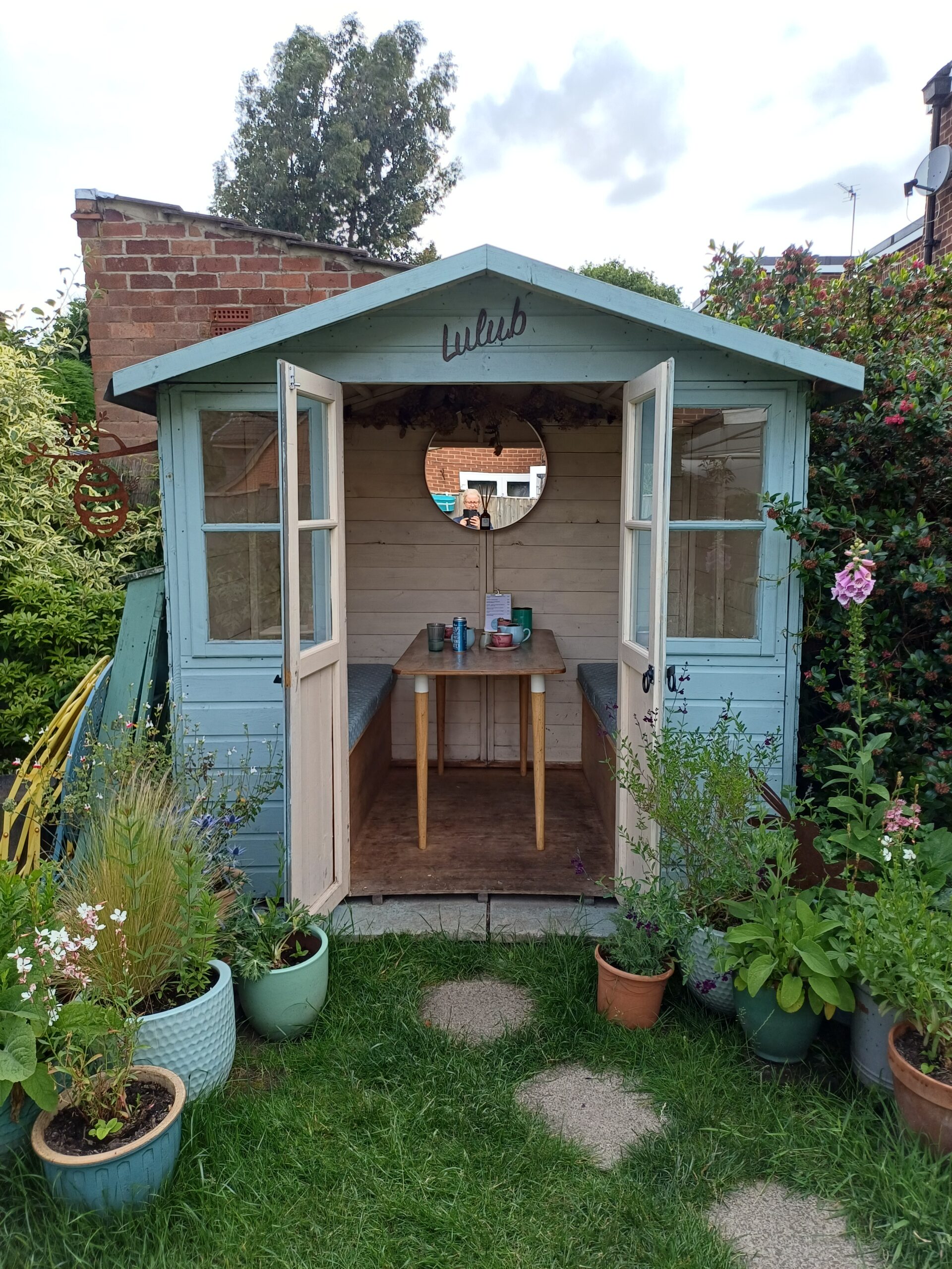 Pretty blue garden room with its doors open, table and mirror visible through the doorway