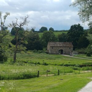 Photograph of stone building in background with foreground of grass, bordered with trees