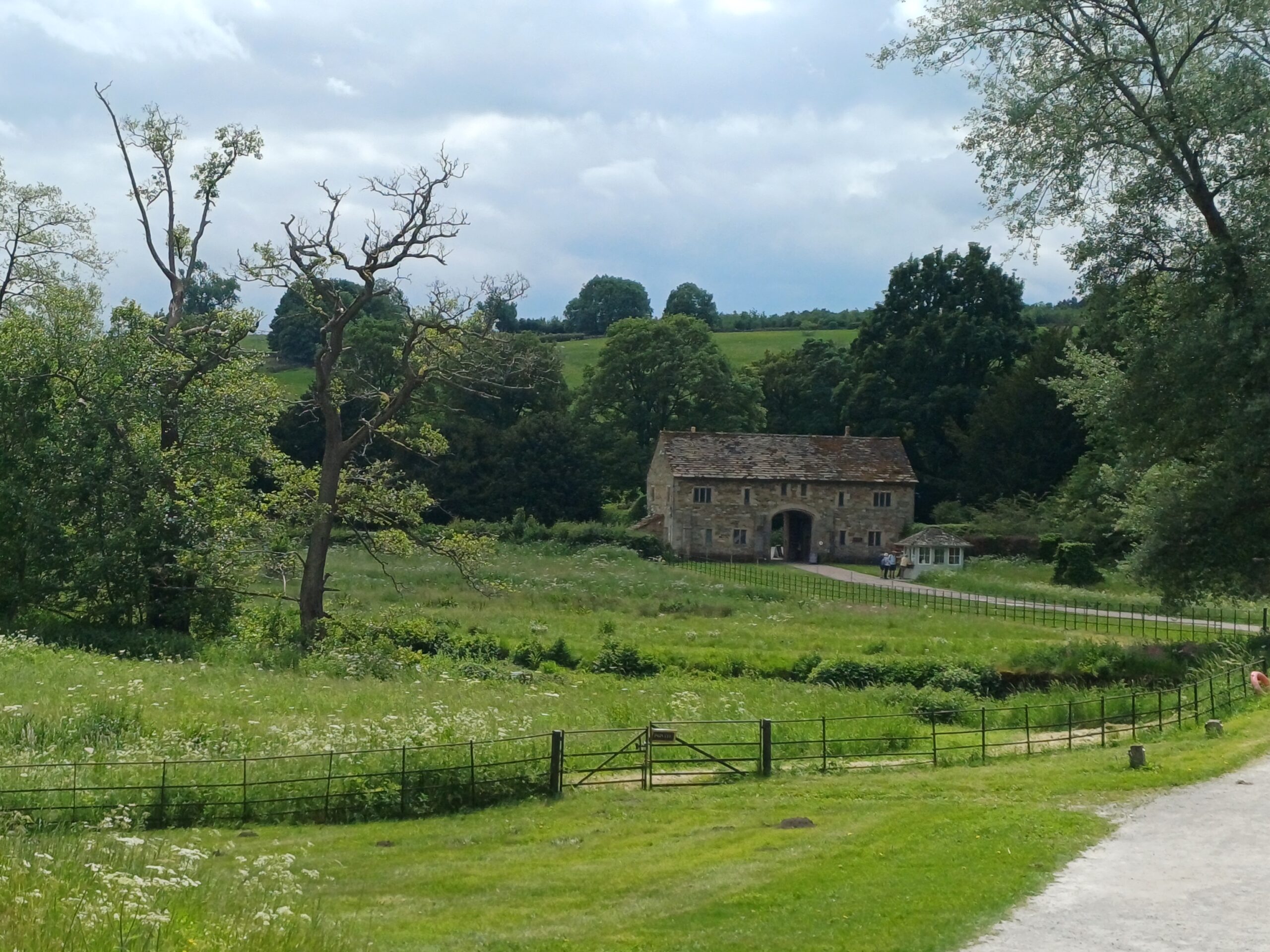 Photograph of stone building in background with foreground of grass, bordered with trees